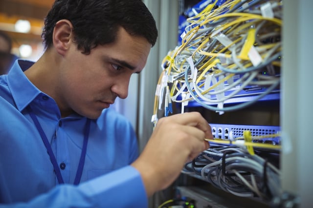 Technician checking cables in a rack mounted server in server room.jpeg